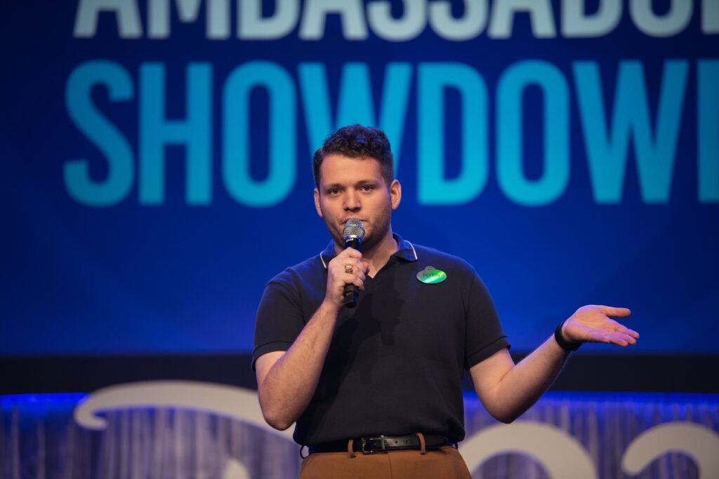 A man delivers a speech into a microphone while standing on stage, engaging the audience with his presentation.