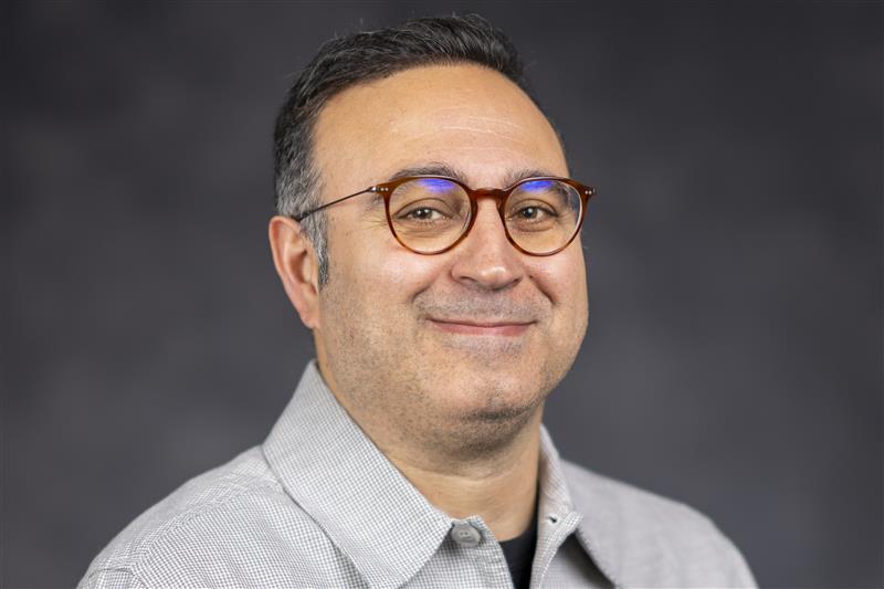 Babak Taheri wears a grey collared shirt and glasses with a brown frame.