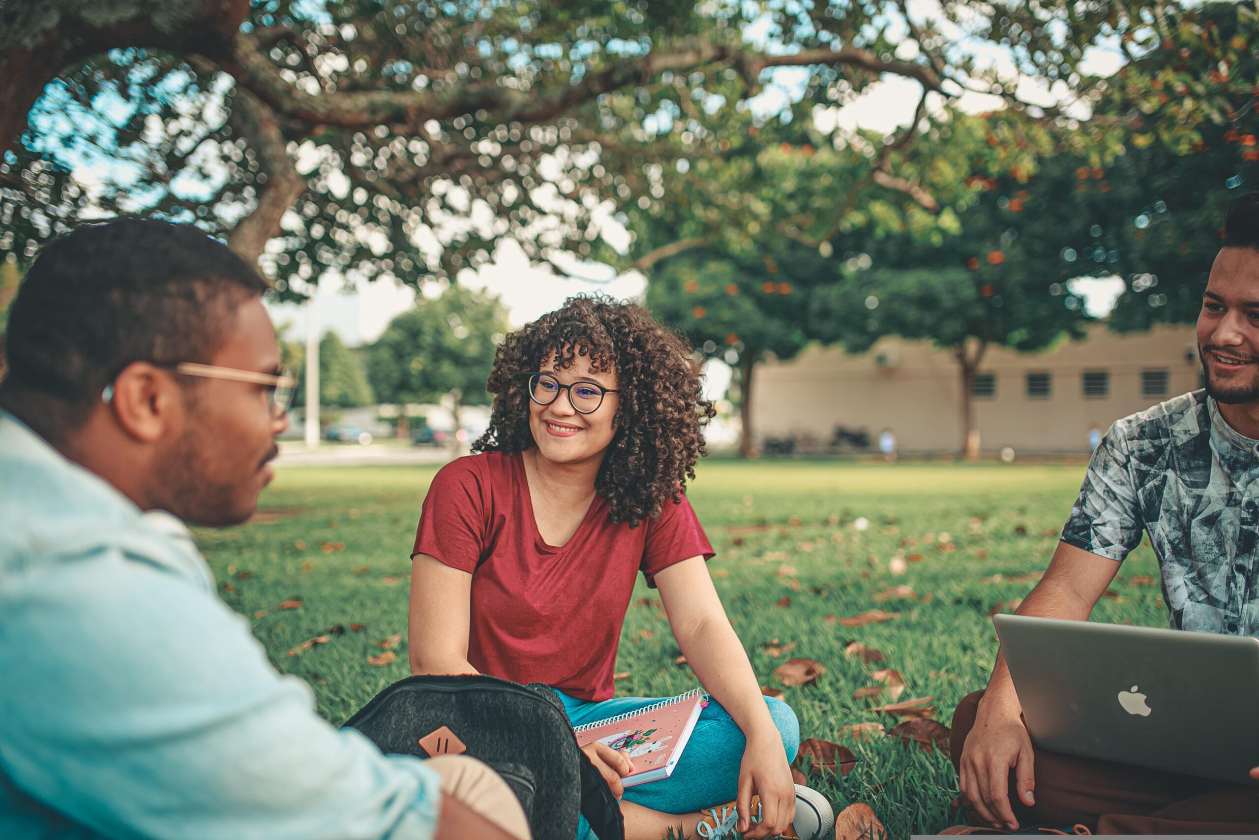 Studnets sitting on a lawn smiling and talking.