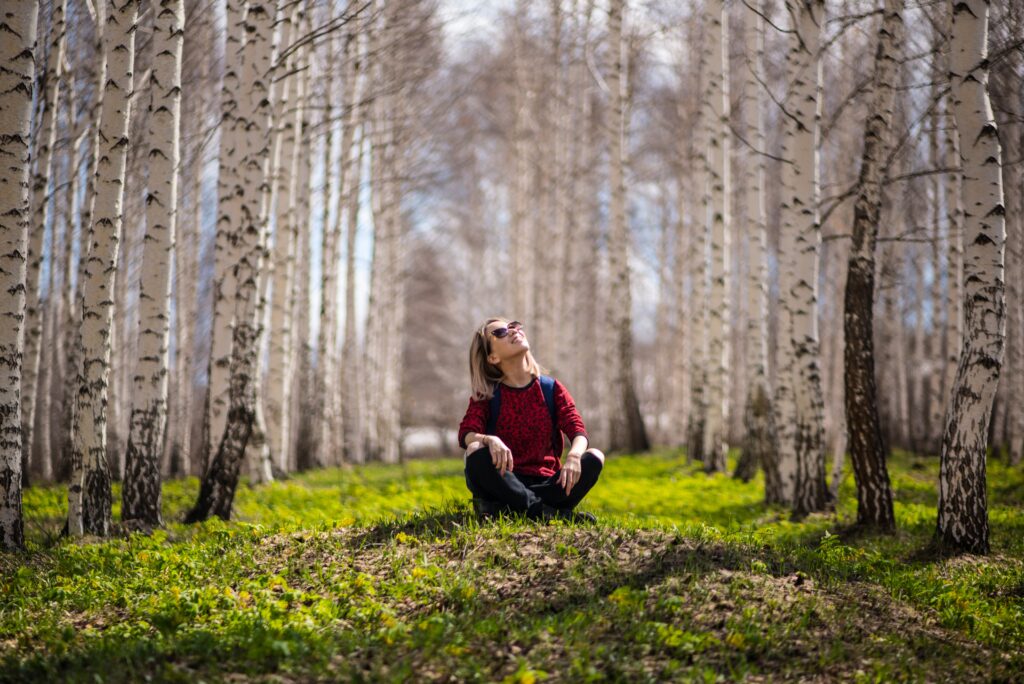 Woman sitting in between two rows of trees looking up.