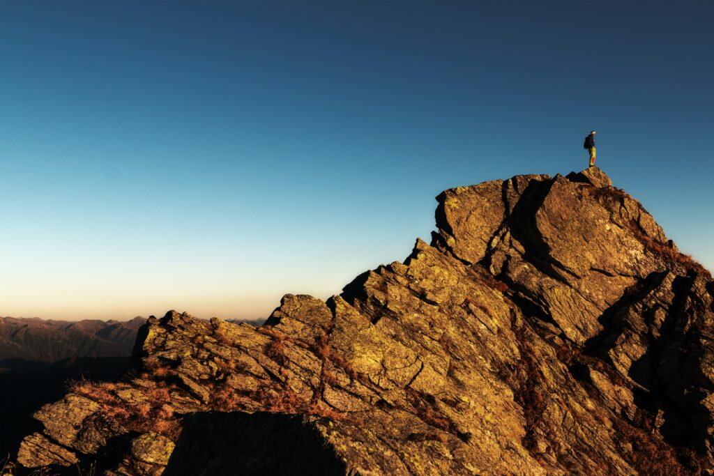 sillouette of a man standing on a rocky formation in the distance.