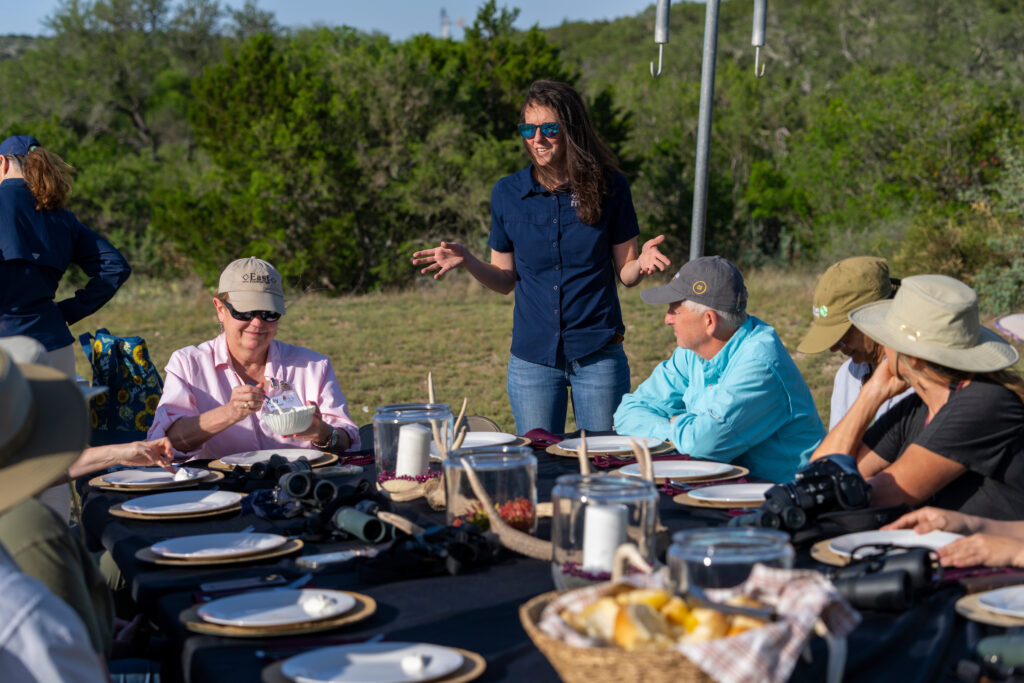 Woman standing at an outdoor dining table giving a speech.