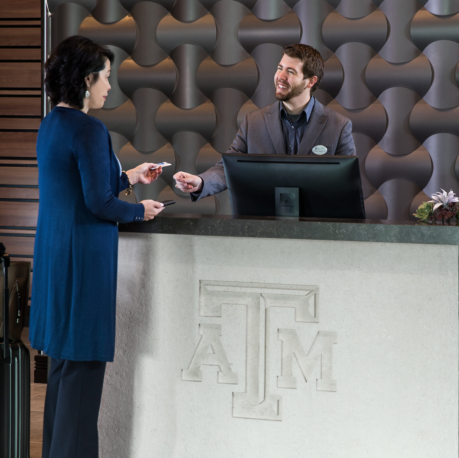 Man at counter with Texas A&M logo smiling and taking a credit card from woman.