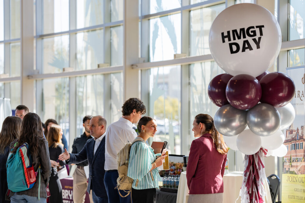 Maroon, silver and white balloons with one saying HMGT Day on it greet students and industry professionals mixing in a room