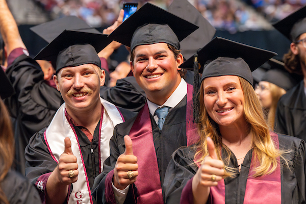 Students in graduation robes and hats giving a thumbs-up